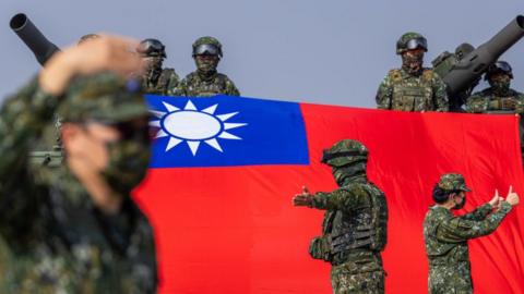 Taiwan soldiers flank a tank draped with the Taiwanese flag.