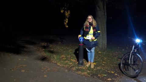 Jennifer Huygens with her bicycle in a a dark Fairlands Valley Park, Stevenage