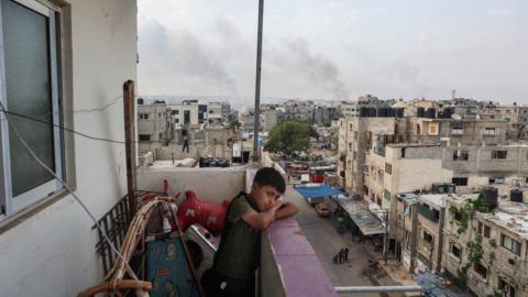 A boy stands on a balcony with a view of billowing smoke due to renewed Israeli strikes in Rafah city in the southern Gaza Strip on May 28, 2024