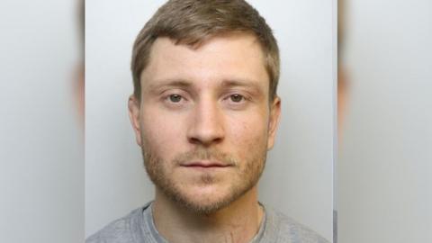 Mugshot of Jones who is wearing a grey top and has brown hair and beard
