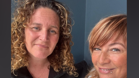 Naomi Alderton and Rachel Hart look directly at the camera and smile. They are taking a selfie. They both had brown hair and blue eyes. 