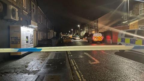 Police cordon and two police vans in a dark residential street.