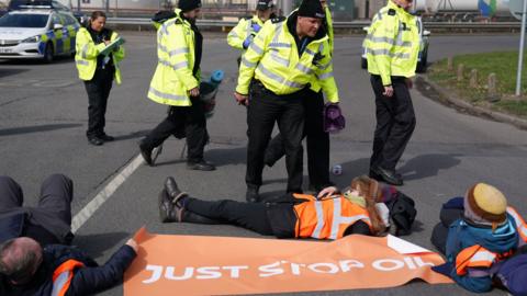 Police officers look at activists from Just Stop Oil taking part in a blockade at the Kingsbury Oil Terminal, Warwickshire