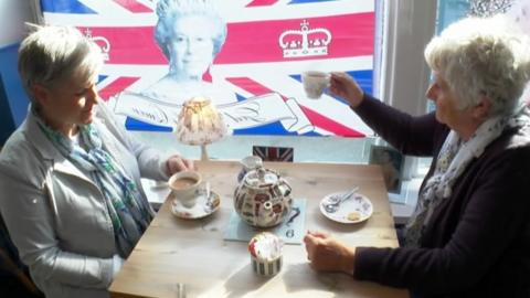 Two ladies sat next to a Queen Elizabeth II flag