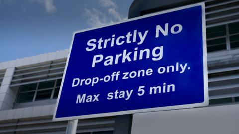 A blue 'Strictly No Parking' sign outside an airport
