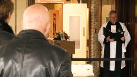 Vicar conducting a funeral service outside a chapel