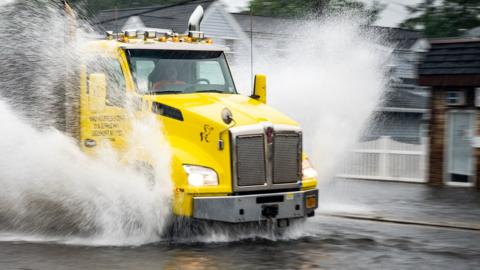 Yellow truck drives through flooded street in Lindenhurst, New York, on 9 July 2021