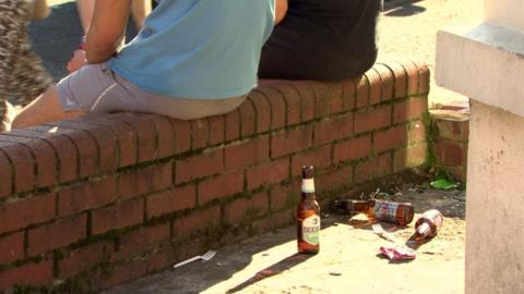 Two young men sitting on a wall with broken beer bottles nearby