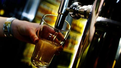 A person pulls a draught beer in a pub. Liquid is pictured pouring into a clear glass from a tap.