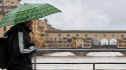 Person with umbrella looking at swollen river in Florence