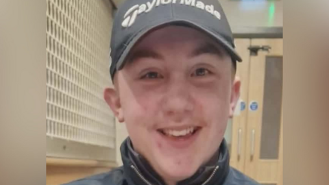 A teenage boy who wears a cap smiles indoors.