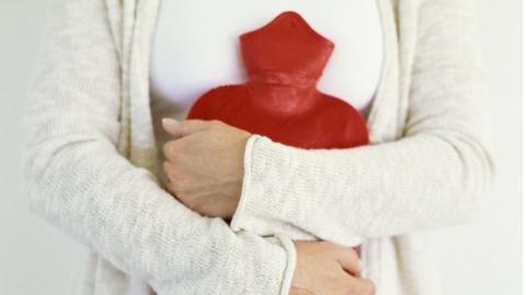 Woman holds hot water bottle to her stomach