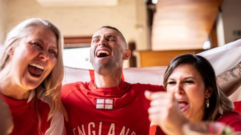 Three England fans gather together in celebration.