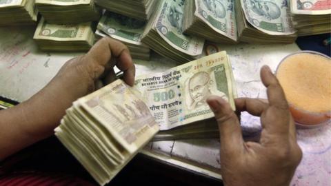 An employee counts Indian currency notes at a cash counter inside a bank