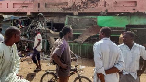People walk past a building riddled with bullet holes at a market hit by shelling in the south of Khartoum - Thursday 1 June 2023