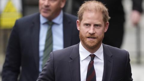 Prince Harry wearing a dark suit with a maroon tie.