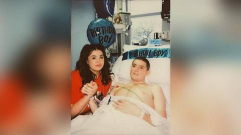 Man in hospital bet holding girlfriend's hand with birthday balloon