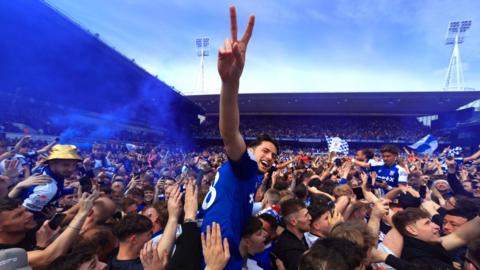 Lewis Travis, player for Ipswich Town, on the shoulders of fans in the crown of the stadium making a peace sign