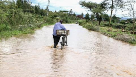 A man pushes his bicycle in a flooded road in Rongai, Nakuru County,