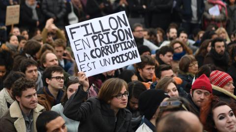 A man holds a placard reading 'Fillon to prison, corruption is a poison' a he sits in place de la Republique in Paris, on February 19, 2017