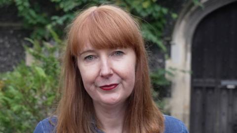 Elise Burns, a woman with auburn hair, wearing a denim outfit 