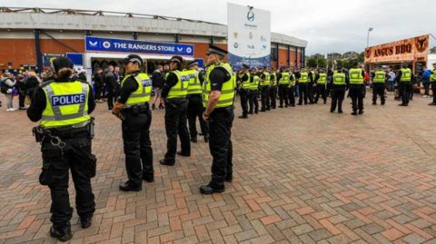 A line of police officers form a human barrier in front of Rangers supporters standing outside Hampden stadium