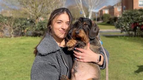 A woman holds a black and brown sausage dog