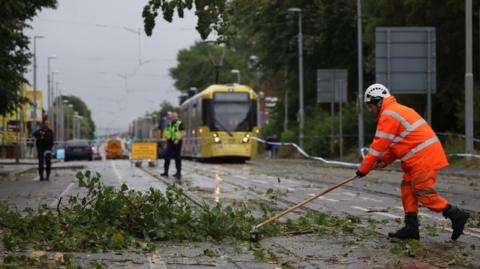 A worker begins to remove fallen tree branches after strong winds brought by Storm Lilian brought down trees blocking roads and tram routes in Manchester, Britain