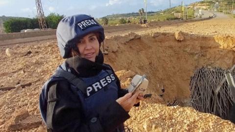 Photo of Al Akhbar journalist Amal Khalil, wearing a press jacket and helmet, reporting near a destroyed bridge in Qasmiyeh.