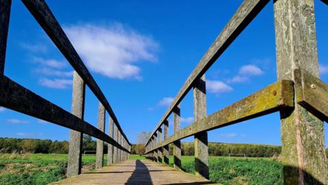 Mainly blue sky above a footbridge crossing a field 