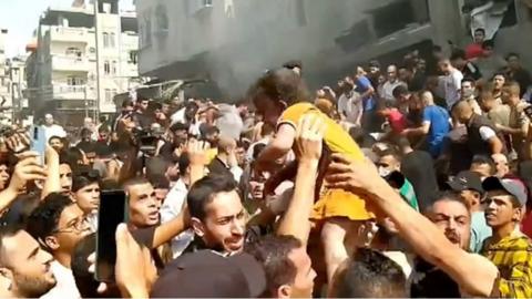 A young girl in a yellow dress is passed through the crowd