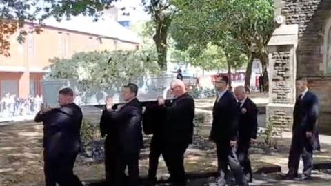 Pallbearears carrying a white coffin carrying white flowers out of a church