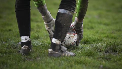 Grassroots football - a green pitch with a goal keeper picking up a football