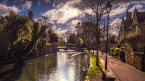The centre of Bourton-on-the-Water showing houses in the sunshine either side of a canal