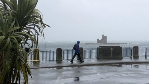 Man walking by Bottle Neck car park in stormy weather
