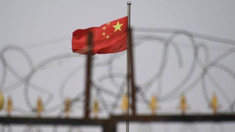 This photo taken on June 4, 2019 shows the Chinese flag behind razor wire at a housing compound in Yangisar, south of Kashgar,