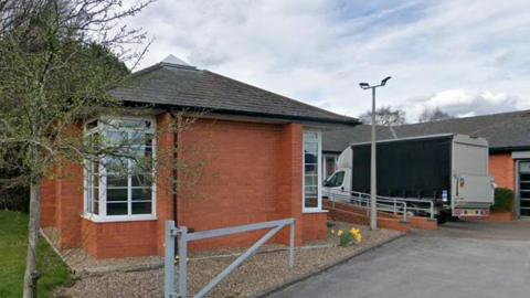 A brick building which was previously an office, with a delivery vehicle parked in front of the site
