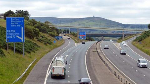 Vehicles on either side of the M65 at a slip road junction, with Darwen Hill and the Jubilee Tower on the summit in the background