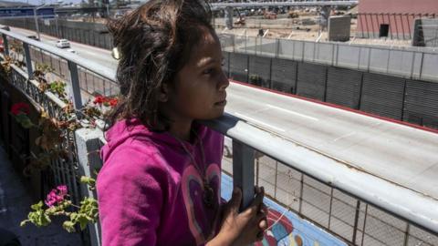 A young migrant girl looks on to the US border