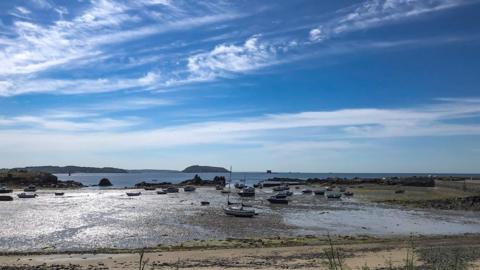 Bright blue sky with fluffy white clouds above an inlet in Guernsey