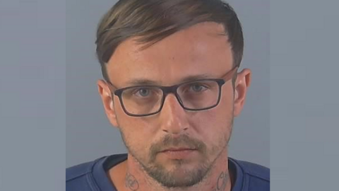 A police custody image of Kieran Bond. He has glasses, straight brown hair combed sideways, a short beard and tattoos on his neck.