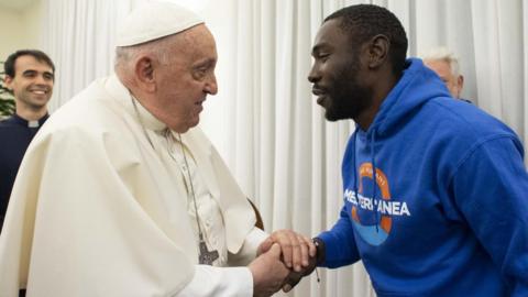 Pope Francis shaking Mbengue Nyimbilo Crepin's hand