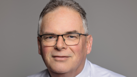 Colin Lang, a man who is looking directly at the camera and smiling. He is wearing a white shirt and red tie.