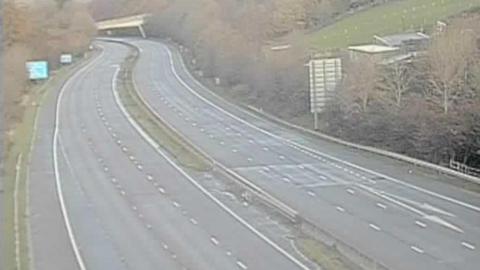 Traffic camera image showing an empty motorway with a bridge in the distance.