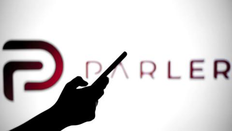 Silhouette of hand holding phone in front of Parler logo.