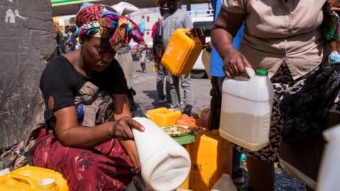 A woman sells gasoline next to a service station, in Port au Prince, Haiti, 24 October 2021