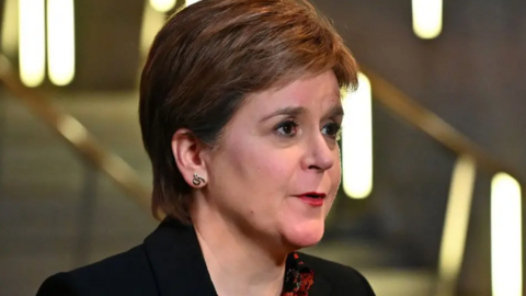 Nicola Sturgeon, with brown hair, wearing a dark jacket, looks to her left in a close-up shot in the Scottish Parliament 