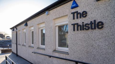 The entrance to the Thistle clinic. The name is in large letters on the wall, and several windows are in a line next to the name.