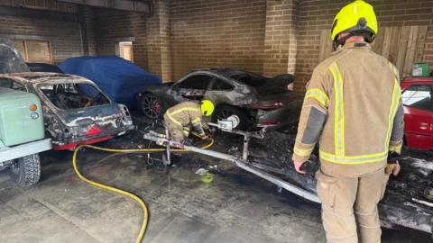 Several singed vehicles and a blackened ground with two firefighters standing around