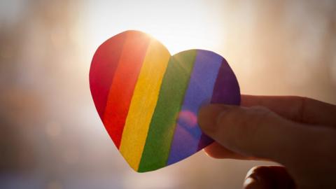 Rainbow coloured paper heart held in hand